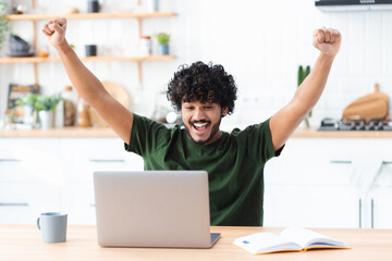 Happy young indian man looking at computer screen making yes gesture, happy with great news, received a nice message in the mail, celebrates success