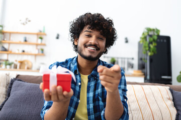 Smiling headshot of smiling Indian man talking online, celebrates a birthday, gives a gift to a friend or loved one. Laughing at camera, making video call at home