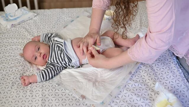 Mother bonding and playing with her baby boy while changing him diaper on the bed