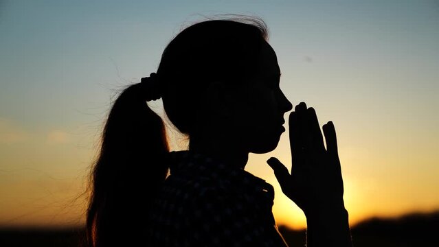 Silhouette Young woman praying at sunset. Christian prayer in nature. Morning prayer of girl outdoors. Freedom of religion. Era of mercy, kindness, love. Path of soul to God through prayer.