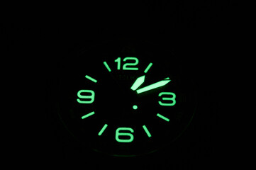 A closeup of the wristwatch neon clock face glowing in the dark on the blank background