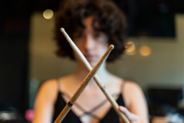 Defocused portrait of a young woman with curly hair playing drums with drumsticks