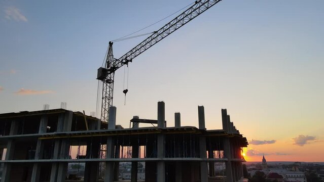 Tower lifting crane and high residential apartment building with monolithic frame under construction at sunset. Real estate development