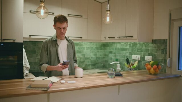 Redhead man drinking coffee and using smartphone and ipods in the kitchen at home
