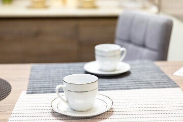 Two tea or coffee cups with saucers on the kitchen table. The topic of waiting for breakfast