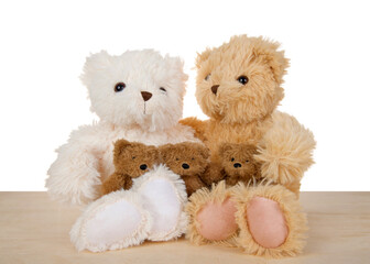Close up of one tan and one white teddy bear sitting side by side on light wood floor, three little baby bears in their laps. Isolated on white.