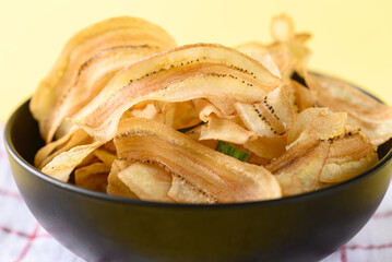 Banana chips or banana crisps in black bowl on yellow background, Delicious snack
