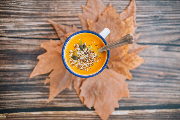 Vegan pumpkin cream in an enameled mug and leaves on wooden background