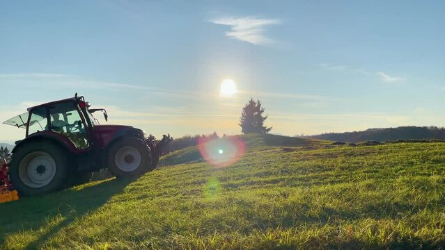 LENS FLARE: Unrecognizable male farmer drives a tractor and flips hay on a sunny summer day. Hot summer sunbeams shine on a farmer operating a tractor dry grass and make feed for his farm animals.