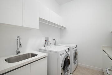 A white laundry room with a sink, white washer and dryer appliances, and a tiled floor.