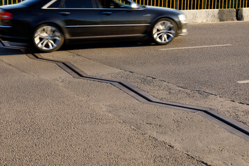 Metallic zigzag edge of drainage channel on asphalt. A fragment of a blurred black car over a...