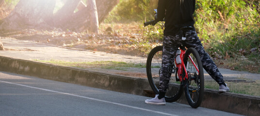 Fototapeta premium man in gym clothes sits on his red bicycle, stopping by the sidewalk.