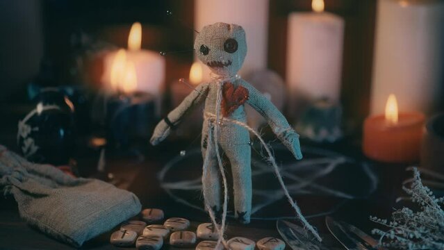 Voodoo doll on table with magical attributes in process of occult ritual and burning candles.