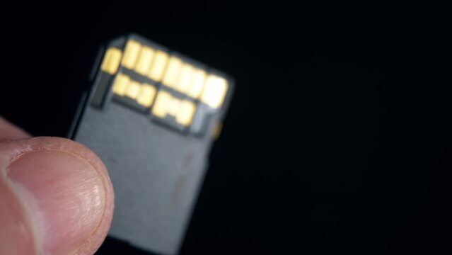 Ultra high speed UHS II SD card in human fingers on dark background. Two rows of gold-plated contacts. View from side of contact area. Fast modern memory storage for video recording. Macro close-up