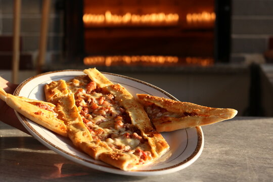 Turkish pide with the vegetables and meet, cut into pieces and with the oven in background