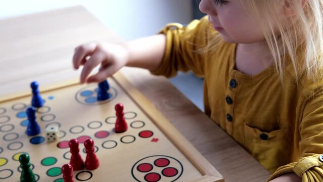 close-up of hands of small child manipulate with wooden figurines of family board game, smart kid, 2-year-old girl is learning to count, Cross and circle game Parcheesi, foreground focus