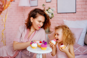 Obraz na płótnie Canvas Happy mother and daughter in bed in pink pajamas eating cakes. Happy holiday weekend.