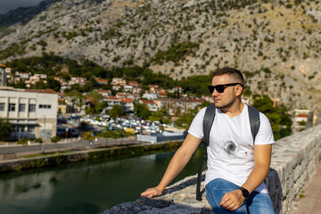 Fototapeta na wymiar Man sits on Kotor old wall Fortification in Montenegro. Unesco world heritage. Europe travel site. Vacation concept. Tourism in adriatic sea. Serbian history of balkans, fort and port buildings..