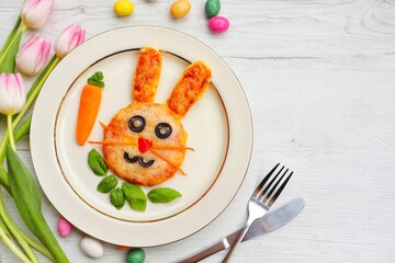 Mini easter bunny pizza made it from pizza crust,pizza sauce,mozzarella cheeses,black olives and carrots on plate with white wood background.Art food idea for kids Easter's party.Top view.Copy space