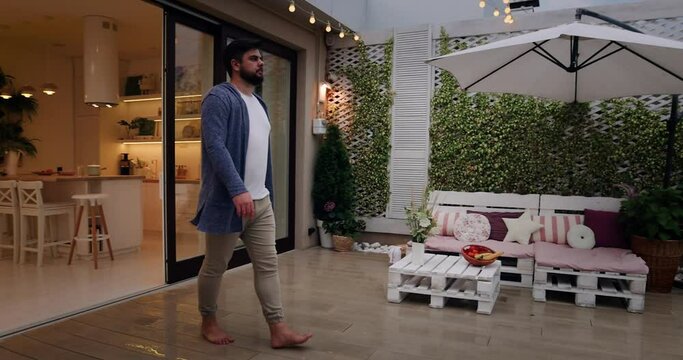 man opens sliding doors, going out on rooftop patio with cozy lounge zone and beautiful landscape
