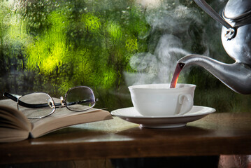 hot coffee pouring into cup on table beside window glass