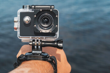 Close-up, Waterproof action camera with mounts on a man's hand. Against the backdrop of the blue water of the sea.