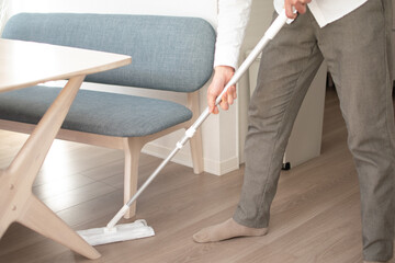 A Japenese young Asian man hoovers the floor using a vacuum cleaner in a house with a desk and two chairs