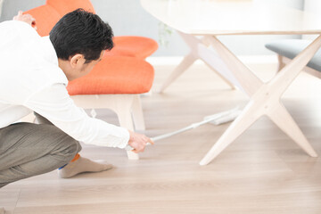 A Japenese young Asian man hoovers the floor using a vacuum cleaner in a house with a desk and two chairs