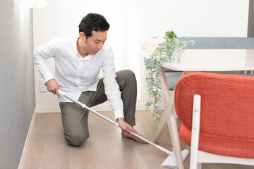 A Japenese young Asian man hoovers the floor using a vacuum cleaner in a house with a desk and two chairs