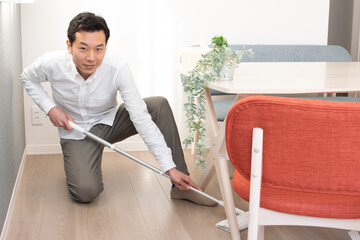A Japenese young Asian man hoovers the floor using a vacuum cleaner in a house with a desk and two chairs