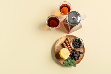 Composition of teapot, glasses with tasty tea and spices on yellow background
