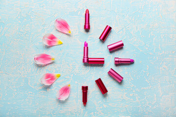 Clock made of lipsticks and flower petals on color background