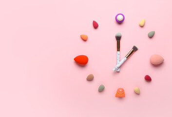 Clock made of makeup sponges, brushes and lip balms on pink background