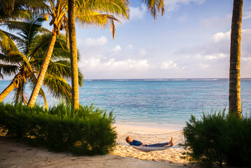 Woman relaxing in a hammock under palm trees on the white sandy beach on the tropical island of Rarotonga, Cook Islands, South Pacific Ocean