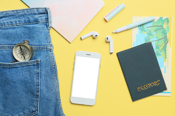 Composition with mobile phone, earphones, passport and compass on yellow background