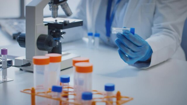 Close up of scientist wearing white coat looking through microscope and making notes whilst holding test tube which he puts on desk to show label kappa - shot in slow motion