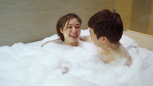 young couple hugging and washing body with foam in bathtub