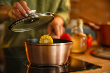 Woman holding sauce pan with corn cobs and opening pot lid in kitchen, closeup