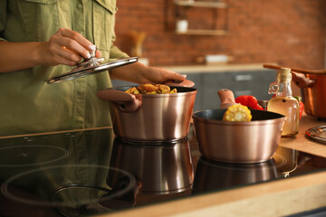 Woman holding cooking pot with vegetable stew and opening lid in kitchen