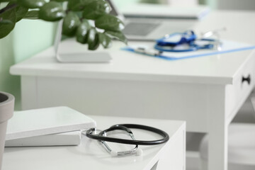 Modern stethoscope and books on shelf in medical office, closeup