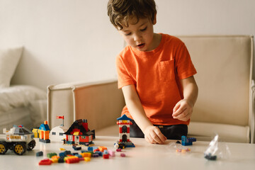 Naklejka premium Cute boy is playing constructor at home. Kid playing block toys in home at nursery. Toddler having fun and building out of bright constructor bricks. Development and Construction Concept
