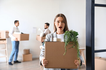 Surprised young woman holding box with personal things in office on moving day