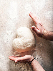 Male hands knead the dough in the shape of a heart. Human hands prepare dough for home baking. Top view. Vertical shot