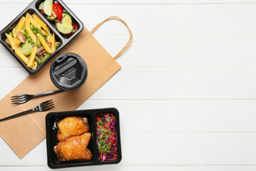 Lunch boxes with food, cup, forks and paper bag on white wooden background
