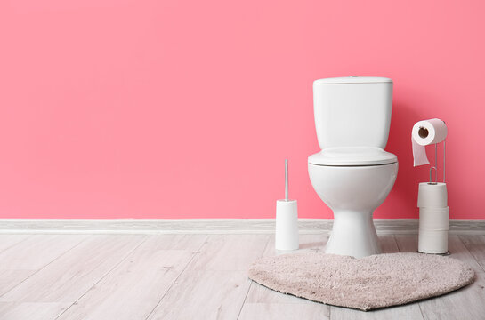 Holder with rolls of paper, brush and toilet bowl near pink wall
