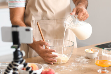 Young man pouring milk into bowl with dough while following cooking video tutorial in kitchen