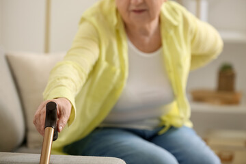 Senior woman with back pain taking walking stick at home, closeup