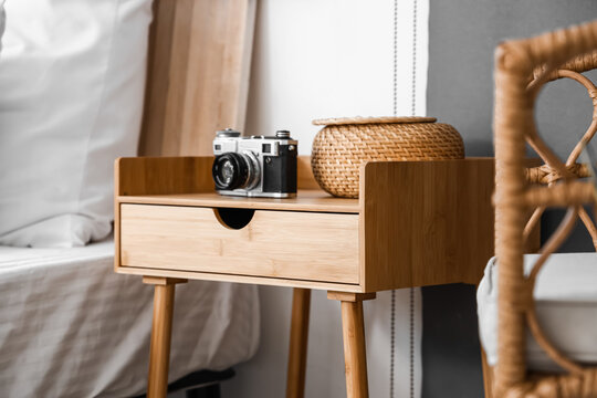 Wooden nightstand with photo camera and wicker basket in light bedroom