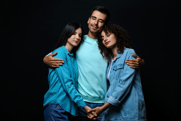Man and two beautiful women on dark background. Polyamory concept