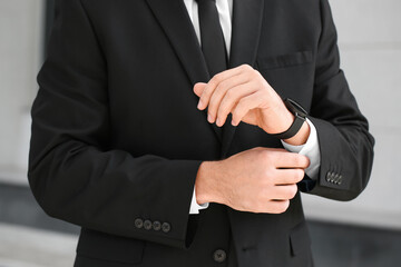 Stylish businessman with smartwatch near office building, closeup